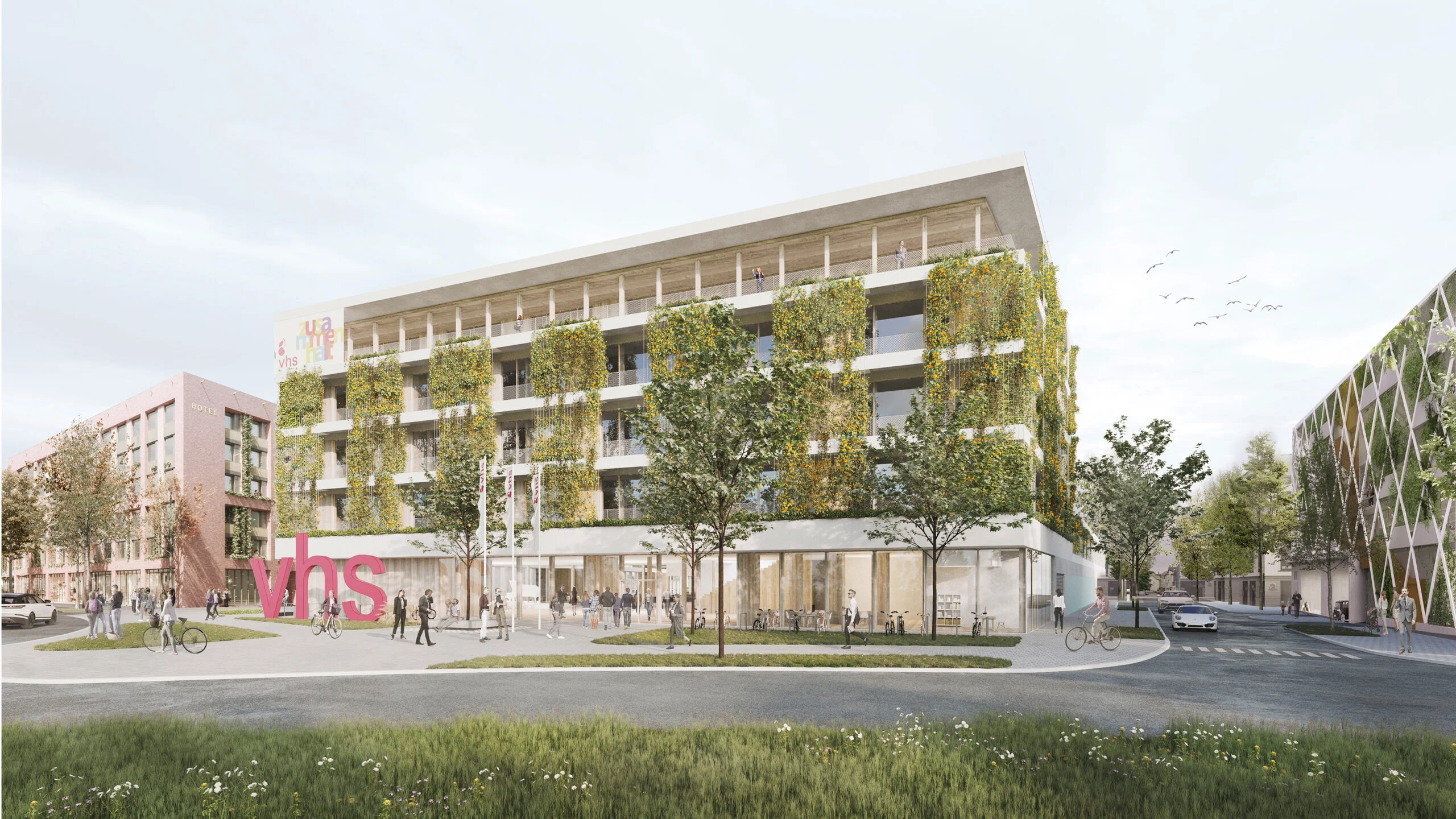 Modernes mehrstöckiges Gebäude mit begrünten Fassaden und Balkonen an einer breiten Fußgängerzone mit mehreren Menschen und einer bunten Skulptur auf einer Rasenfläche.