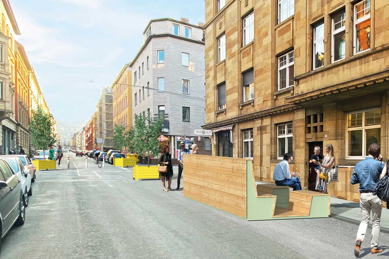 Städtische Straße mit parkenden Autos, Fußgängern und temporären Holzmöbeln auf dem Bürgersteig vor einem historischen Gebäude