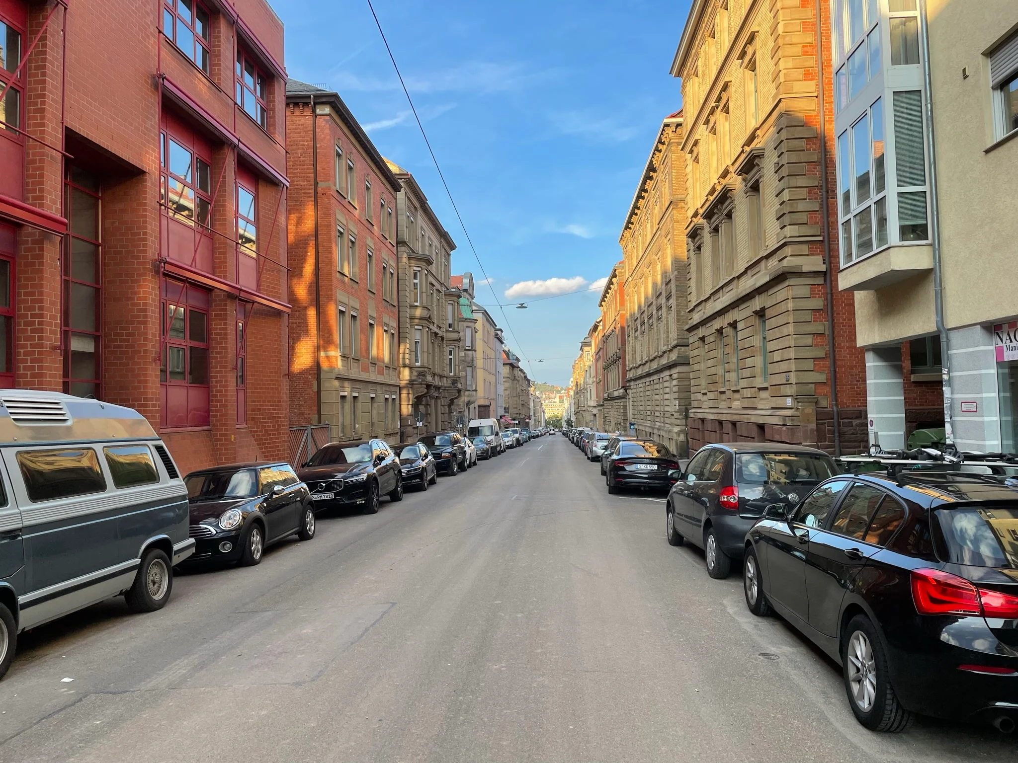 Blick in eine breite Straße mit parkenden Autos auf beiden Seiten und mehrstöckigen Altbauten bei klarem Himmel