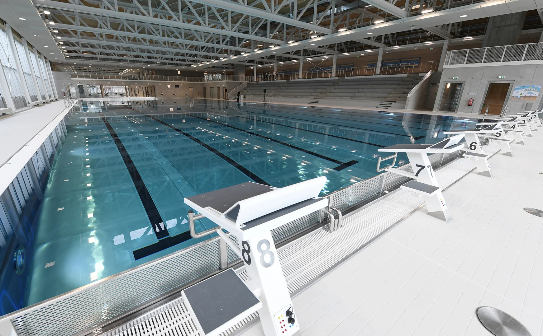 Innenansicht des Sportbads Neckarpark mit Schwimmbecken, Startblöcken und Tribüne.